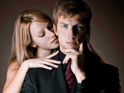 man in suit with woman behind him nuzzling his neck
