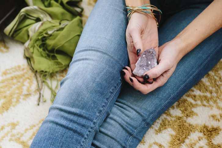 en woman sitting holding a small purple crystal in her hands.