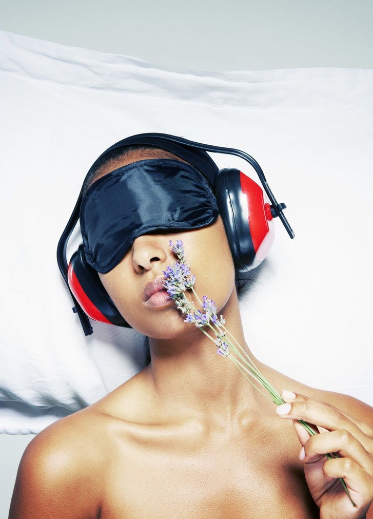 A sleeping woman wearing an eye mask and headphones holding a sprig of lavender